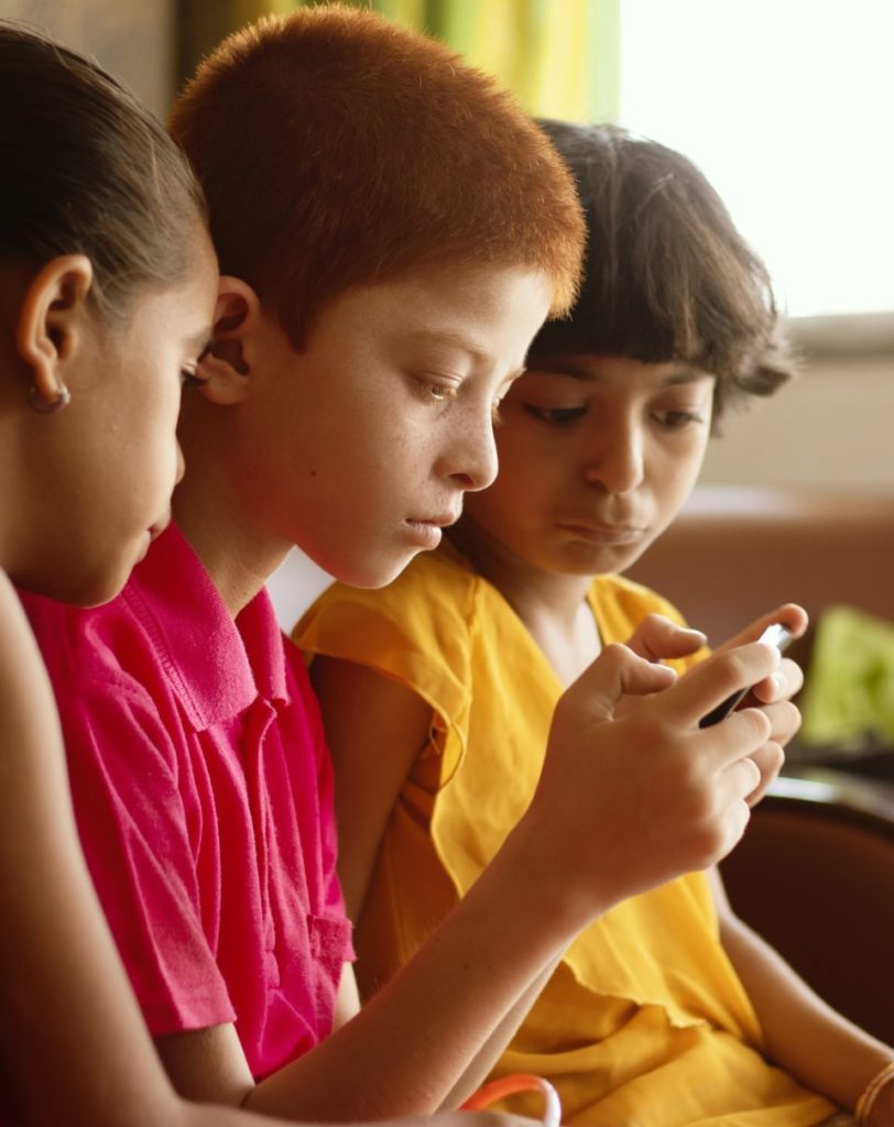 Trois enfants en bas âge en train de regarder l'un d'entre eux jouer sur son téléphone portable