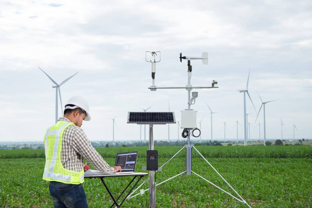 Technicien en train de faire des relevés devant un parc d'éoliennes