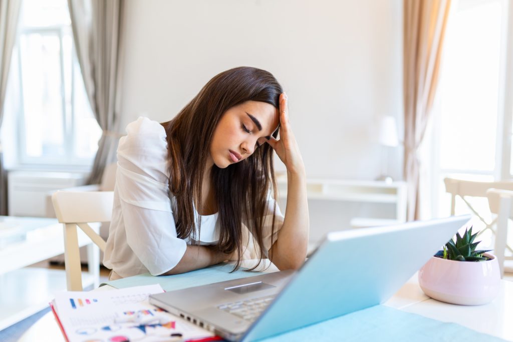 Jeune femme derrière l'écran de son ordinateur portable semblant souffrir de maux de tête ou de fatigue