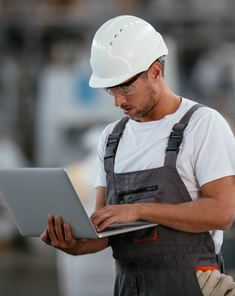 Travailleur dans une usine portant un casque sur la tête et un ordinateur portable dans les mains