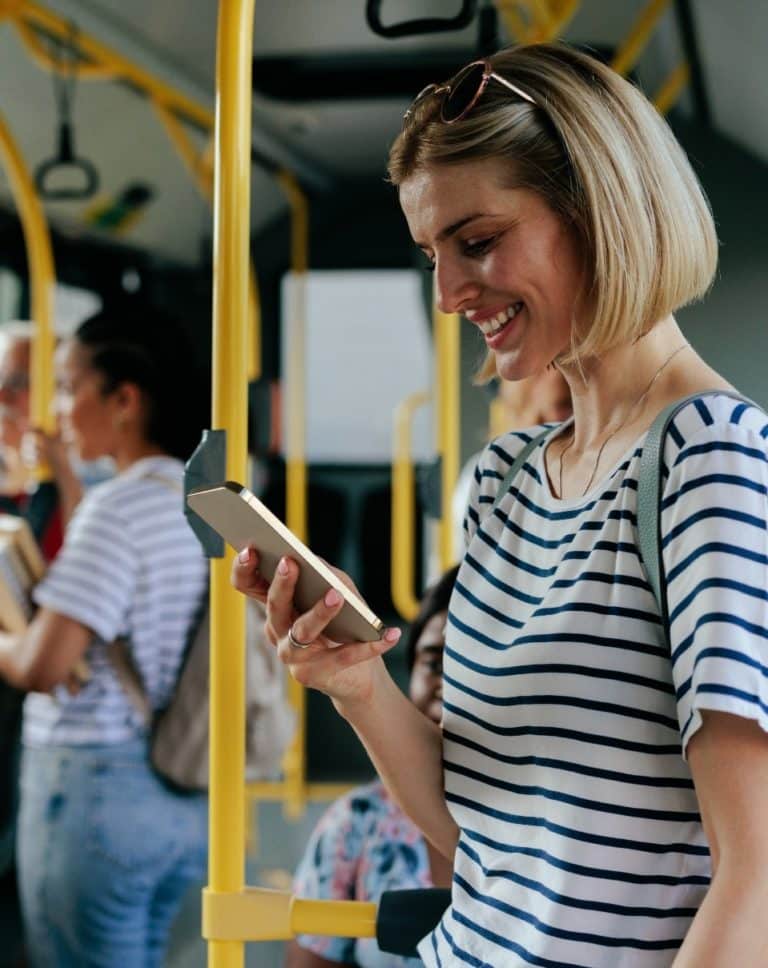 Femme debout dans le bus en train de sourire en regardant l'écran de son téléphone portable
